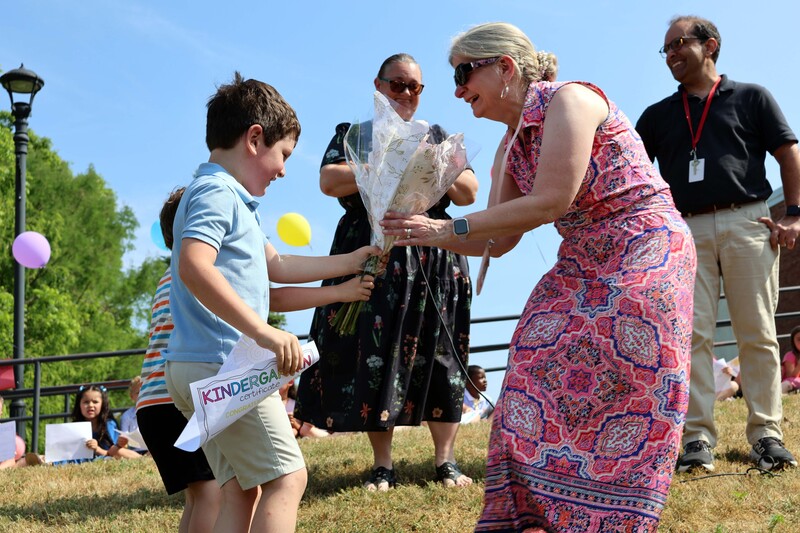 two boys handing woman flowers