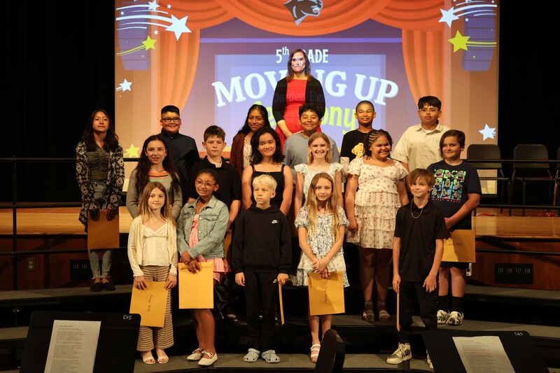 class of 5th graders pose for photo on risers with certificates
