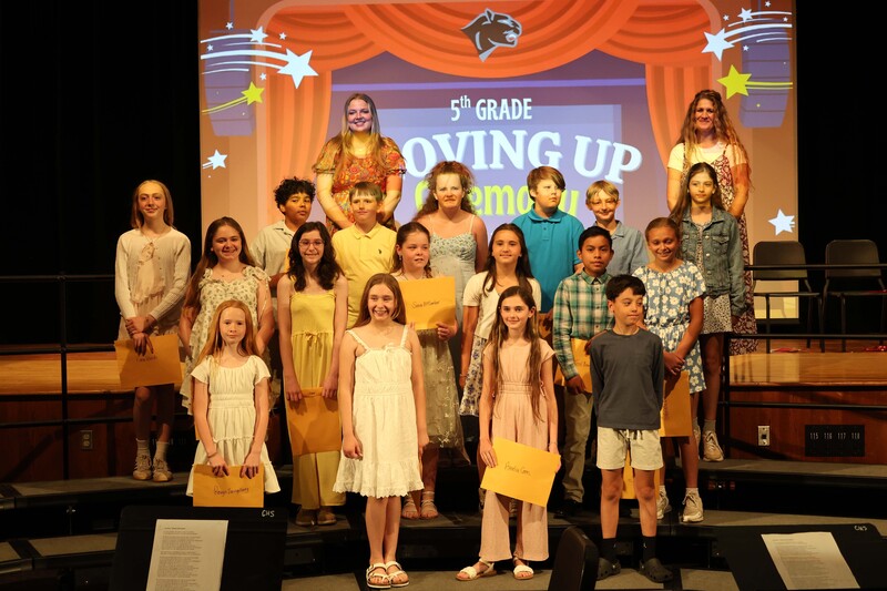class of 5th graders pose for photo on risers with certificates