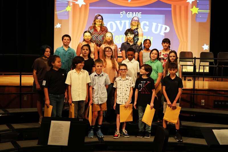 class of 5th graders pose for photo on risers with certificates