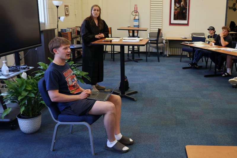 student acting as witness answers questions whil teacher dressed as judge looks on.