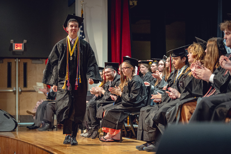 young man in cap and gown walking across stage