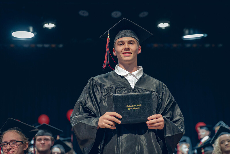 young man in cap and gown posing with diploma