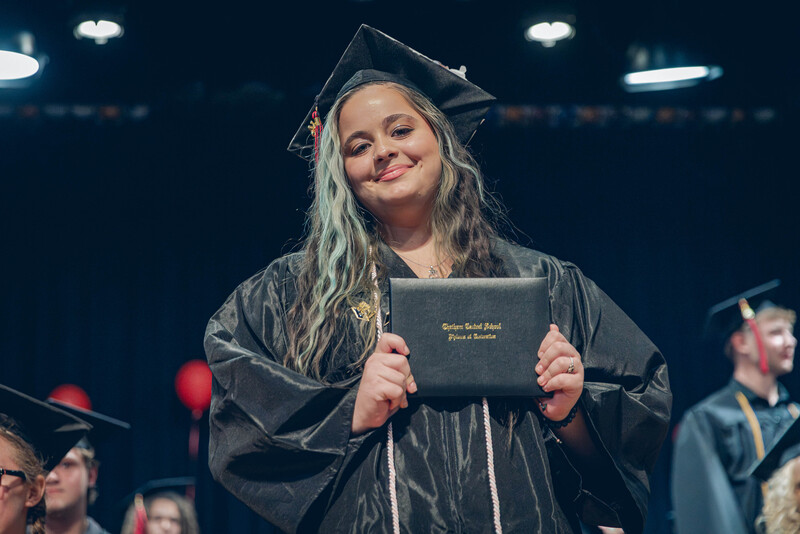 young woman in cap and gown posing with diploma from man in suit on stage
