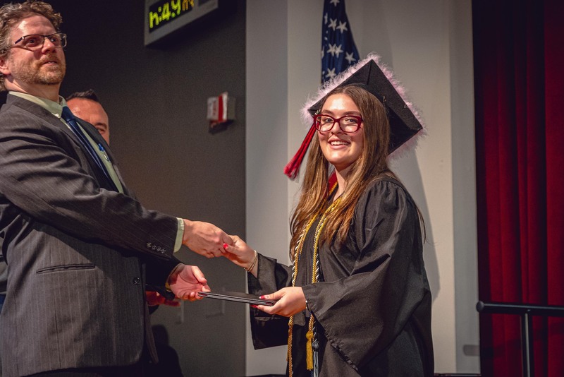 young woman in cap and gown receiving diploma from man in suit on stage