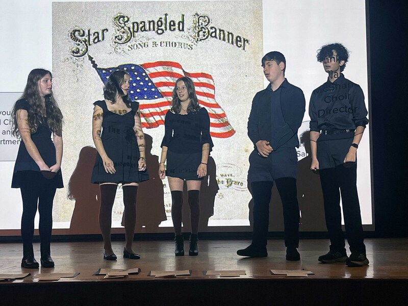 three young women and two men singing on stage 