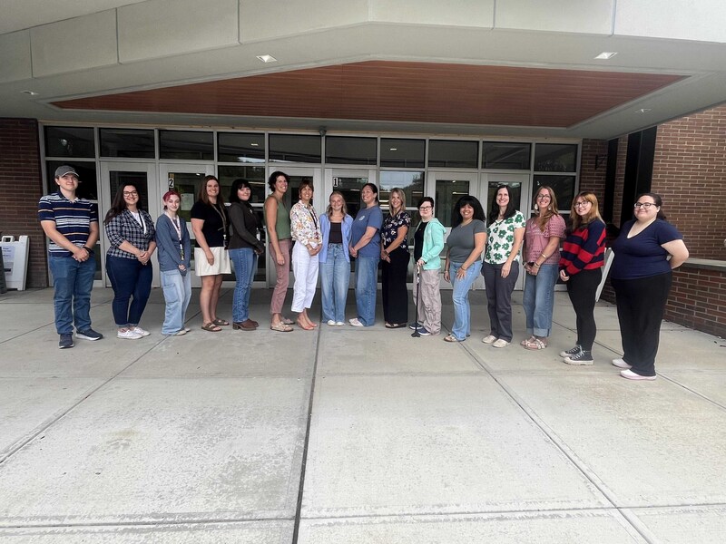 new staff pose for group photo in front of high school entrance