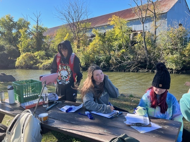 students logging data at picnic table next to river