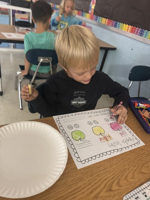 boy coloring in apple on a piece of paper