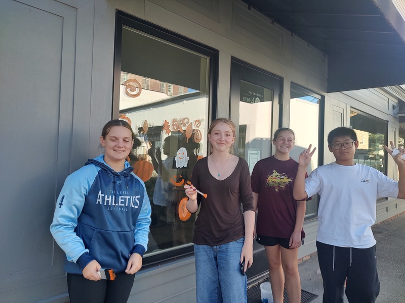four students pose with window painted in Halloween theme