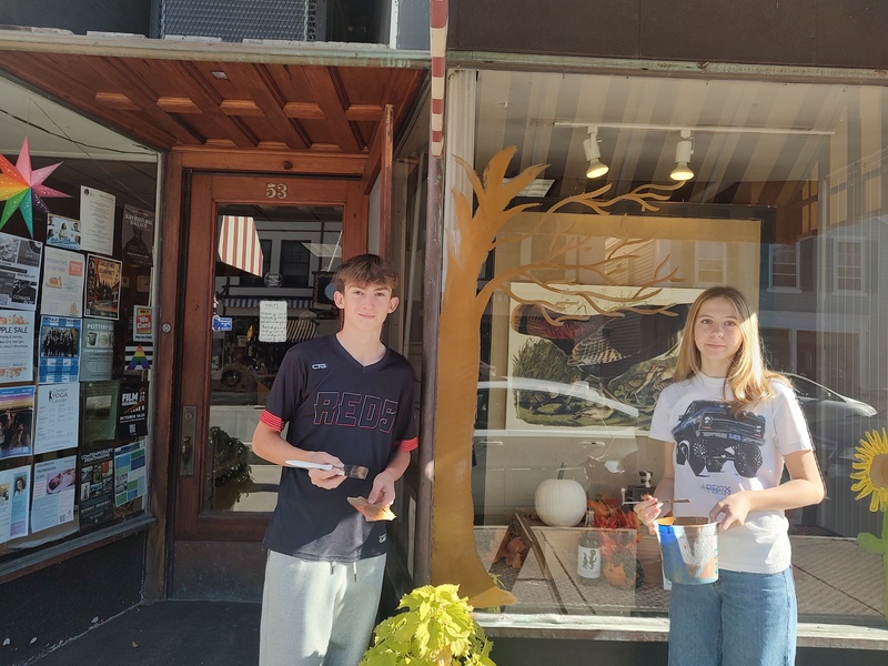 two students pose with window painted in Halloween theme