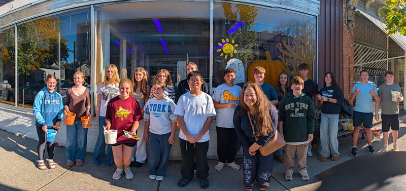 panoramic photo of group of students posing in front of store window painted in fall theme
