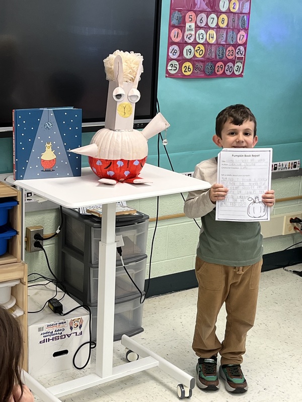 Boy holding book report next to book and decorated pumpkin