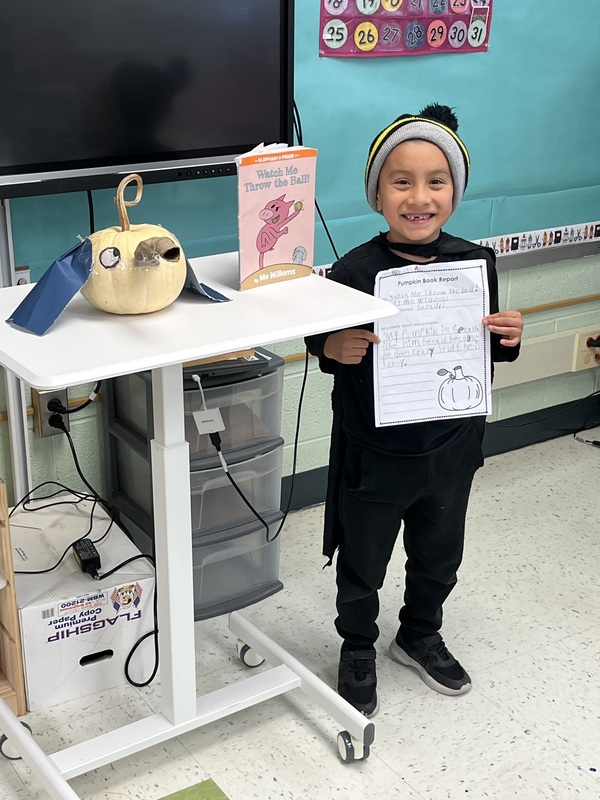 Boy holding book report next to book and decorated pumpkin