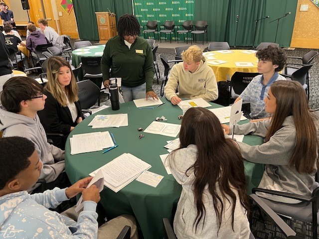 students seated around table in large college room.