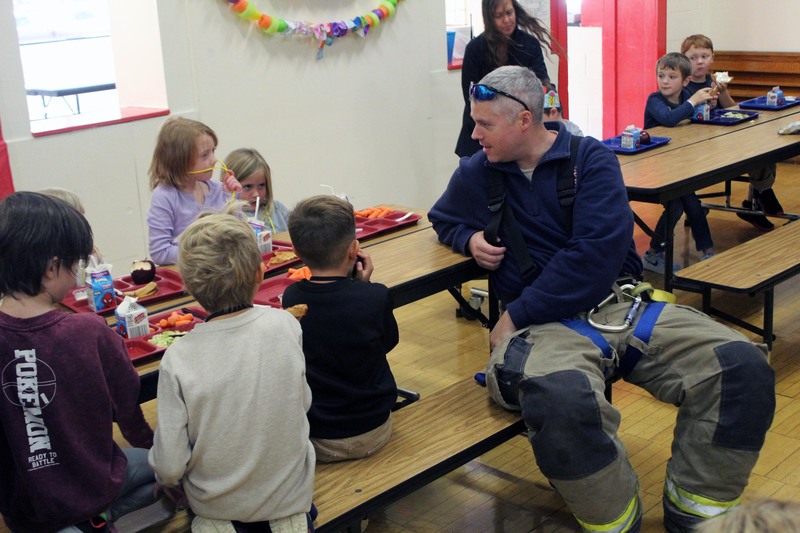 firefighter sitting at cafeteria table with students