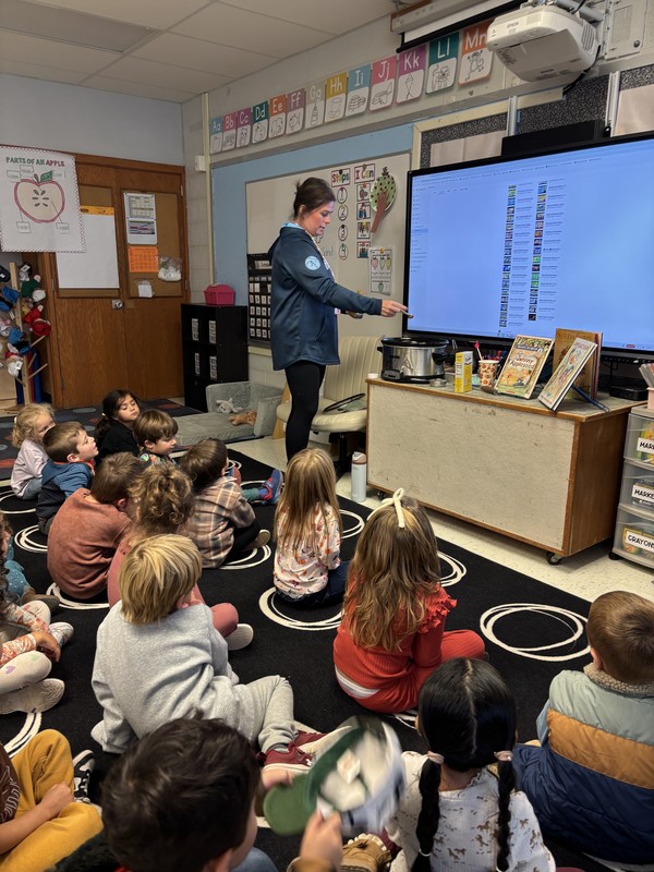 woman pointing to screen in front of seated children