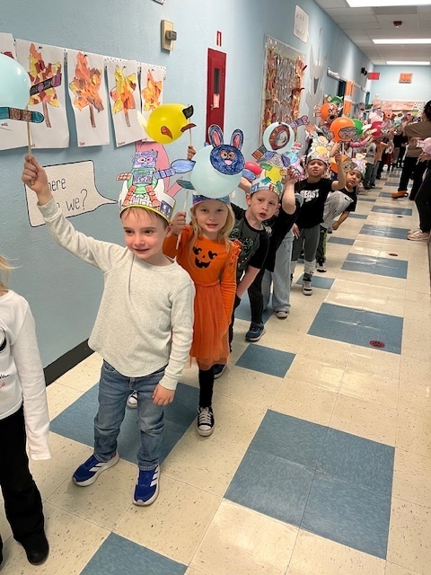 students holding baloons decorated as creatures and walking down the school hallway