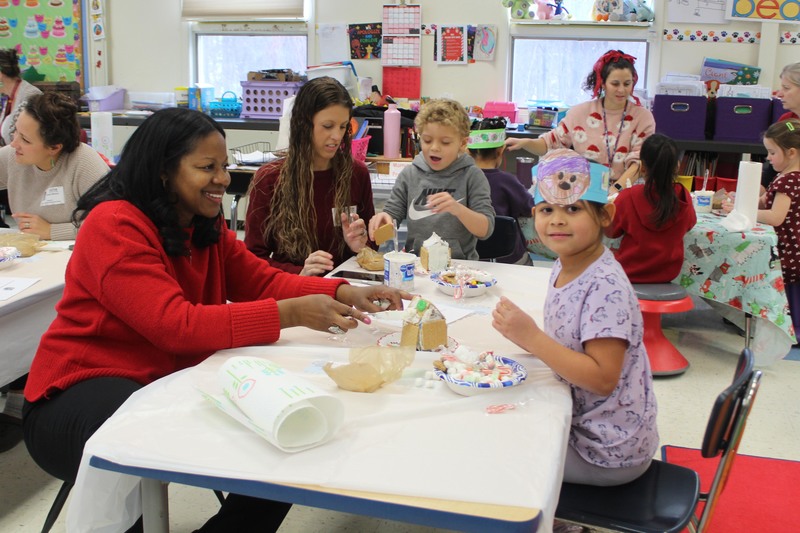 two women, boy, and girl  making gingerbread houses at table