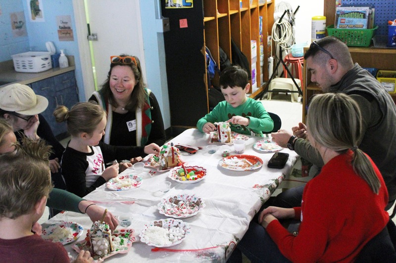 adults and children  making gingerbread houses at table 