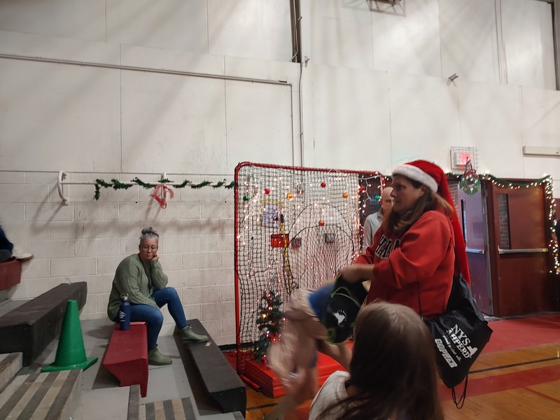 woman in Santa hat throwing candy to students seated in bleachers