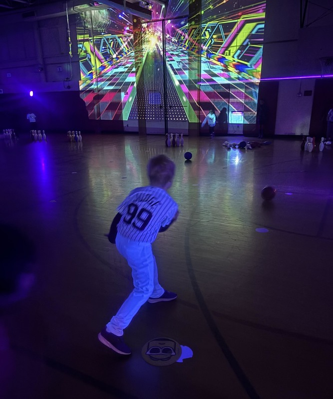 boy bowling in brightly-lit black-lighted gym