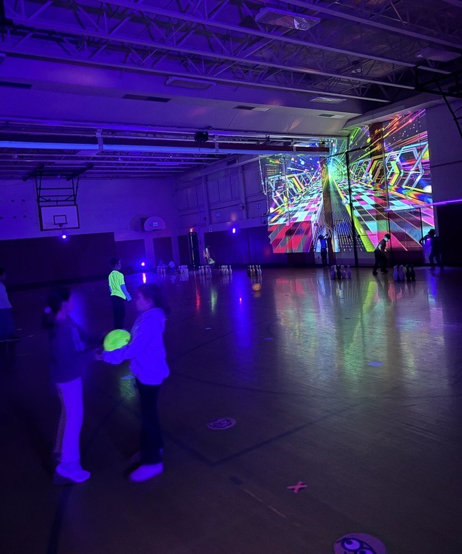 students bowling with glowing bowling balls under blacklights