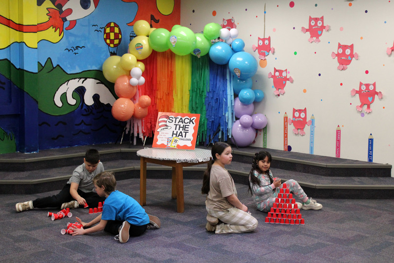 children stackinh cups in front of balloon arch in library