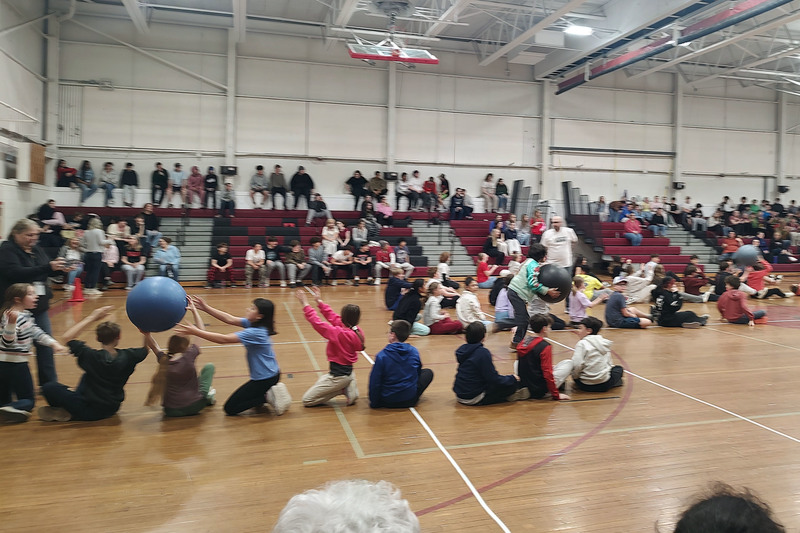 students sitting in line passing large ball overhead