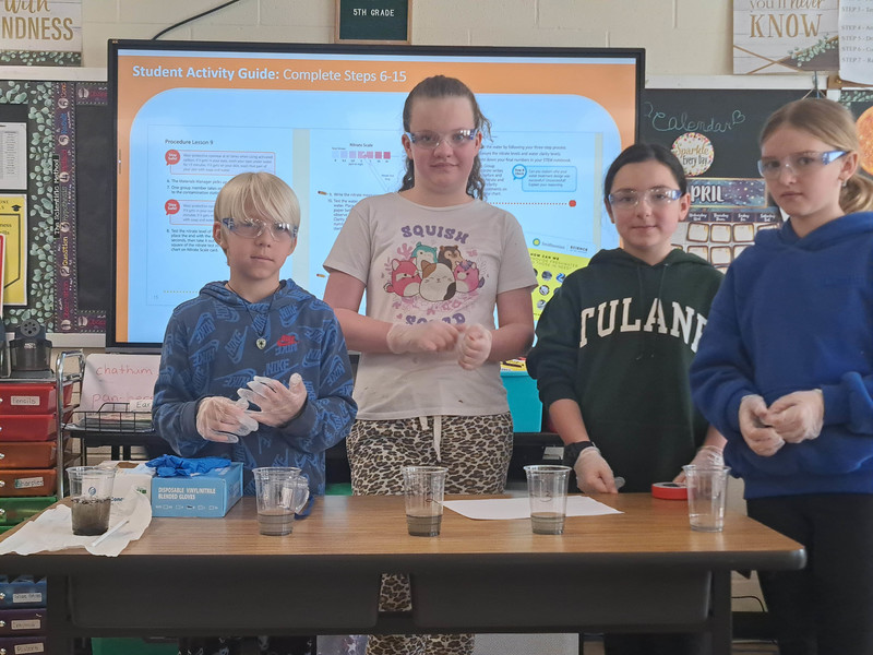 students pose with glasses of water in varying states of clearness