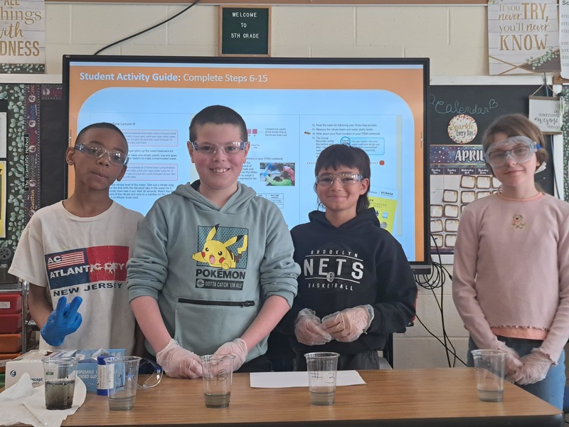 students pose with glasses of water in varying states of clearness