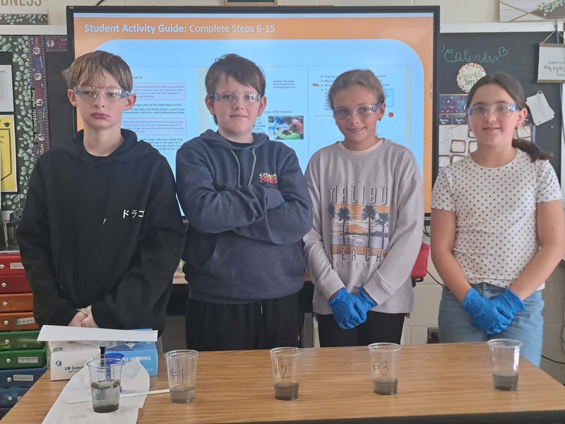 students pose with glasses of water in varying states of clearness
