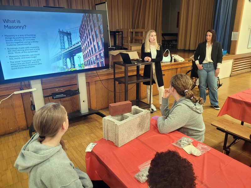 two women talking to students  seated at tables
