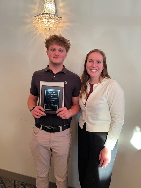 Young man and woman pose for photo with award plaque