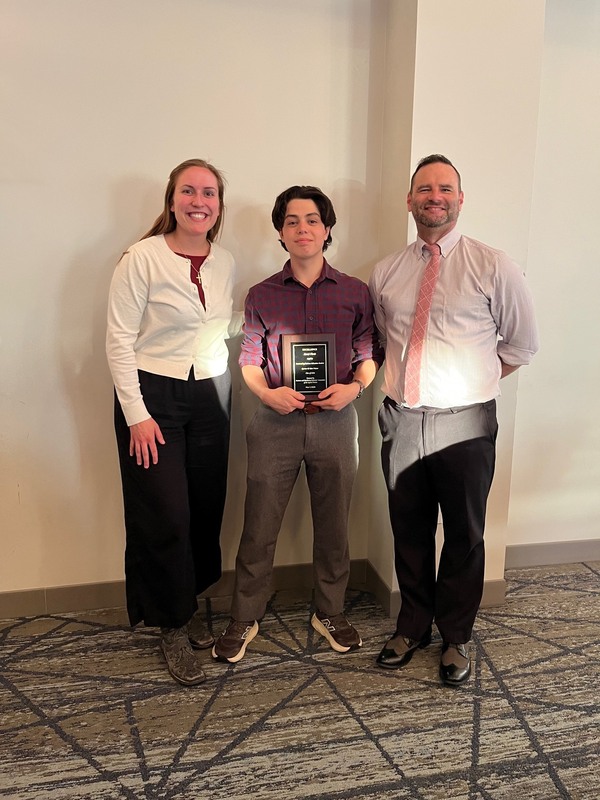 young man holding award plaque poses with woman and man