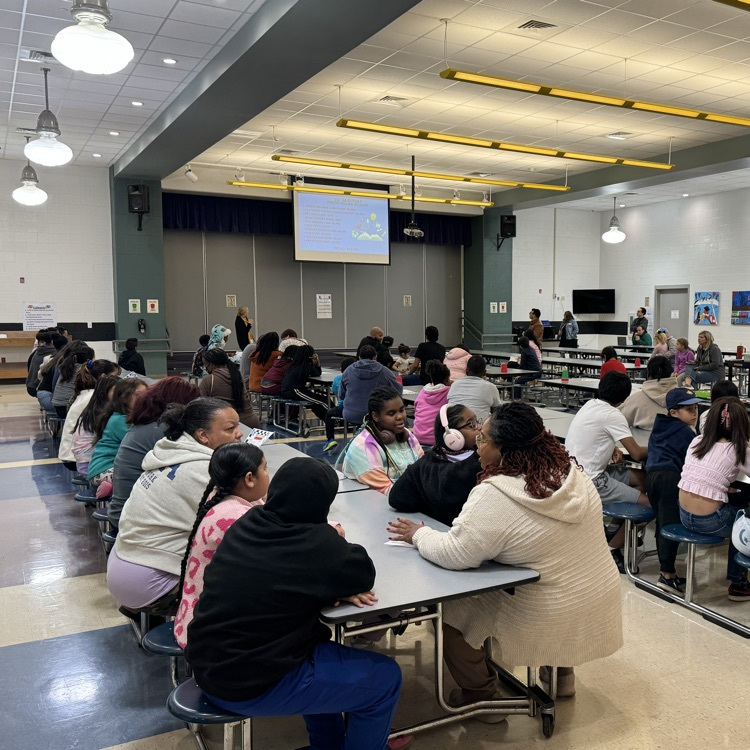 parents and children sitting in a school cafeteria for a meeting