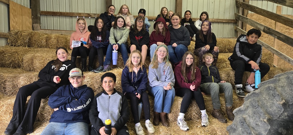 group of student sitting on hay bails at farm