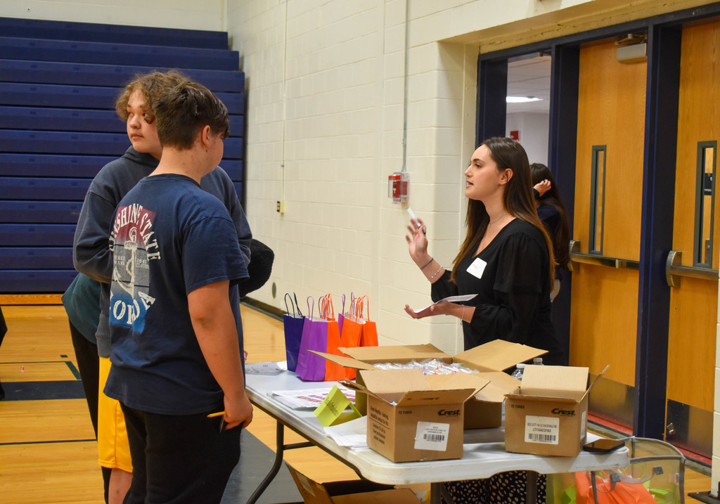students in gym talking with community organization set up at table