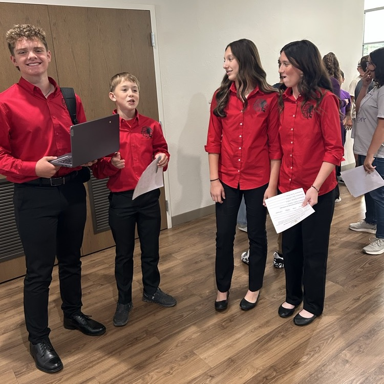 4 students in red shirts. one holding a Chromebook