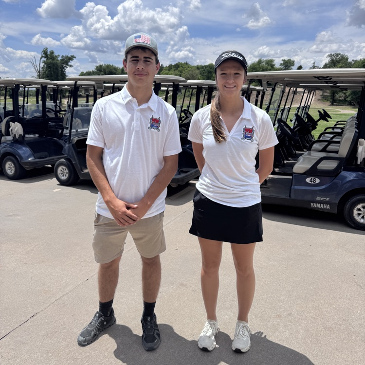 2 students infront of golf carts. they played in the k101 classic golf tournament  