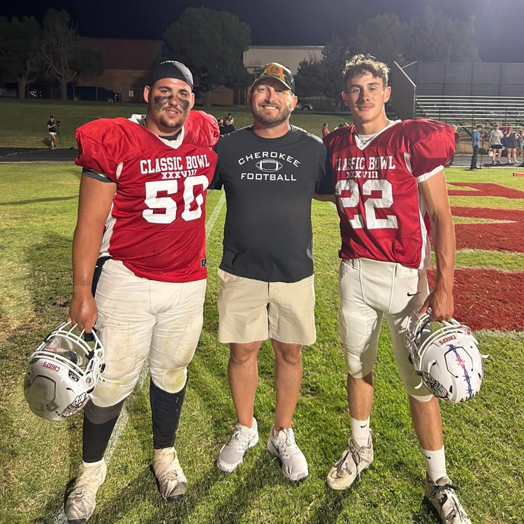 photo of 3 men standing on a football field 2 in uniform