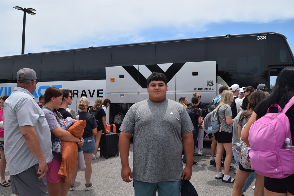 Cherokee student standing in-front of a bus with other parents and students in the background.