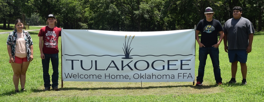 Photo of 4 students standing next to a banner for the FFA Alumni Camp.
