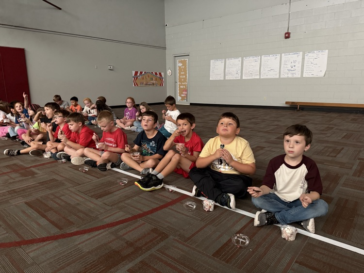 photo students setting on the floor in a gym eating ice cream and watching a movie