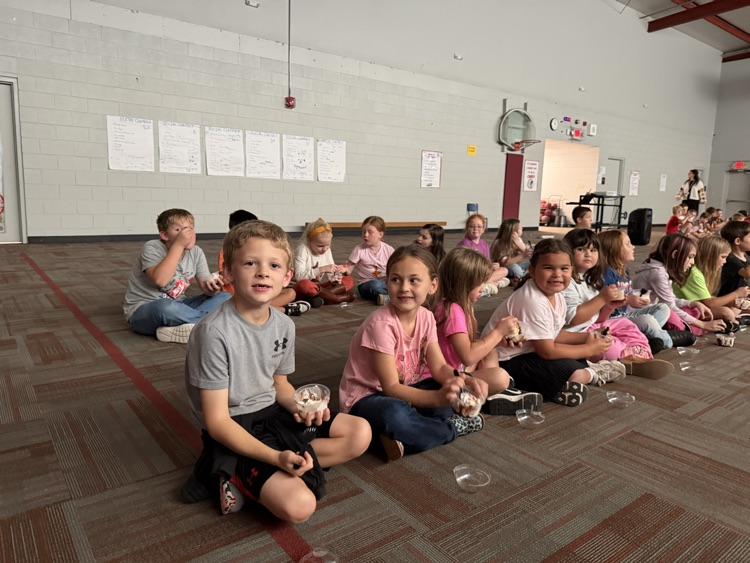 photo students setting on the floor in a gym eating ice cream and watching a movie.