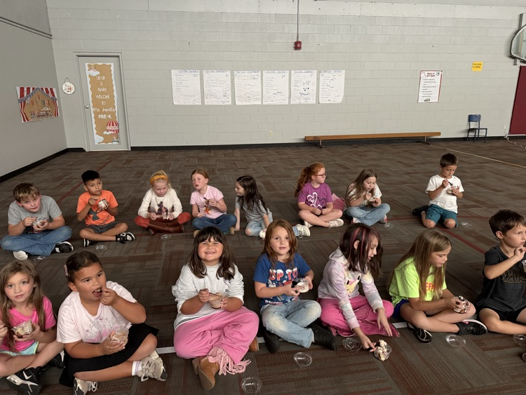photo students setting on the floor in a gym eating ice cream and watching a movie.