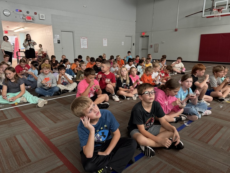 photo students setting on the floor in a gym eating ice cream and watching a movie.