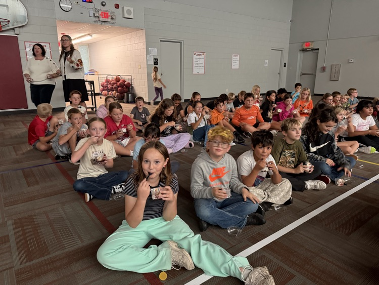 photo students setting on the floor in a gym eating ice cream and watching a movie.