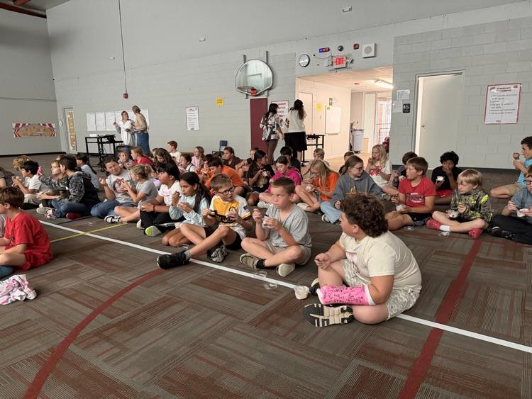 photo students setting on the floor in a gym eating ice cream and watching a movie.