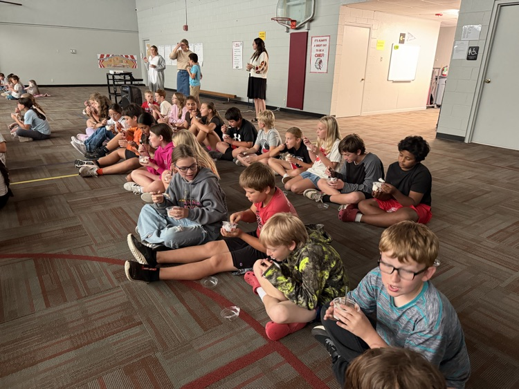 photo students setting on the floor in a gym eating ice cream and watching a movie.